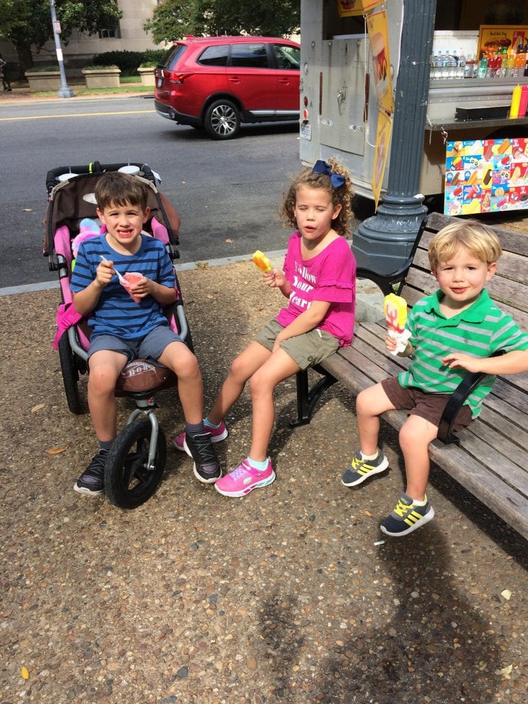 Child sitting in stroller next to 2 children sitting on bench in Washington D.C.
